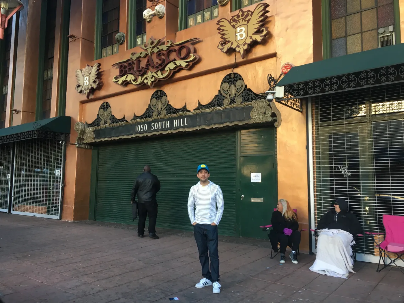 Jimmy Dushku standing outside the Belasco Theatre wearing a blue smiley face hat