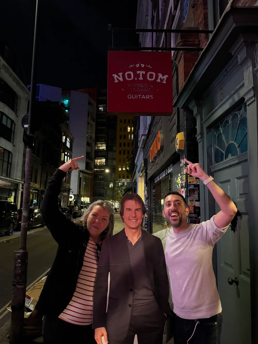 Jimmy Dushku and Jannie posing with a cardboard cutout of Tom Cruise under a guitar shop sign