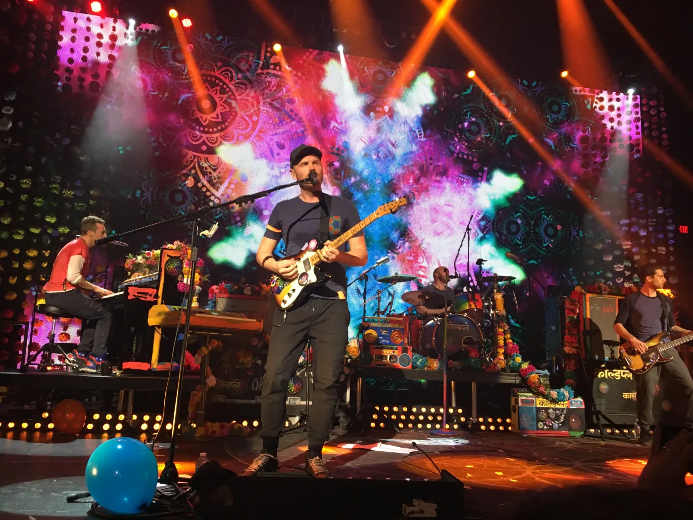 Coldplay performing on stage at the Belasco Theatre with colorful mandala visuals behind them