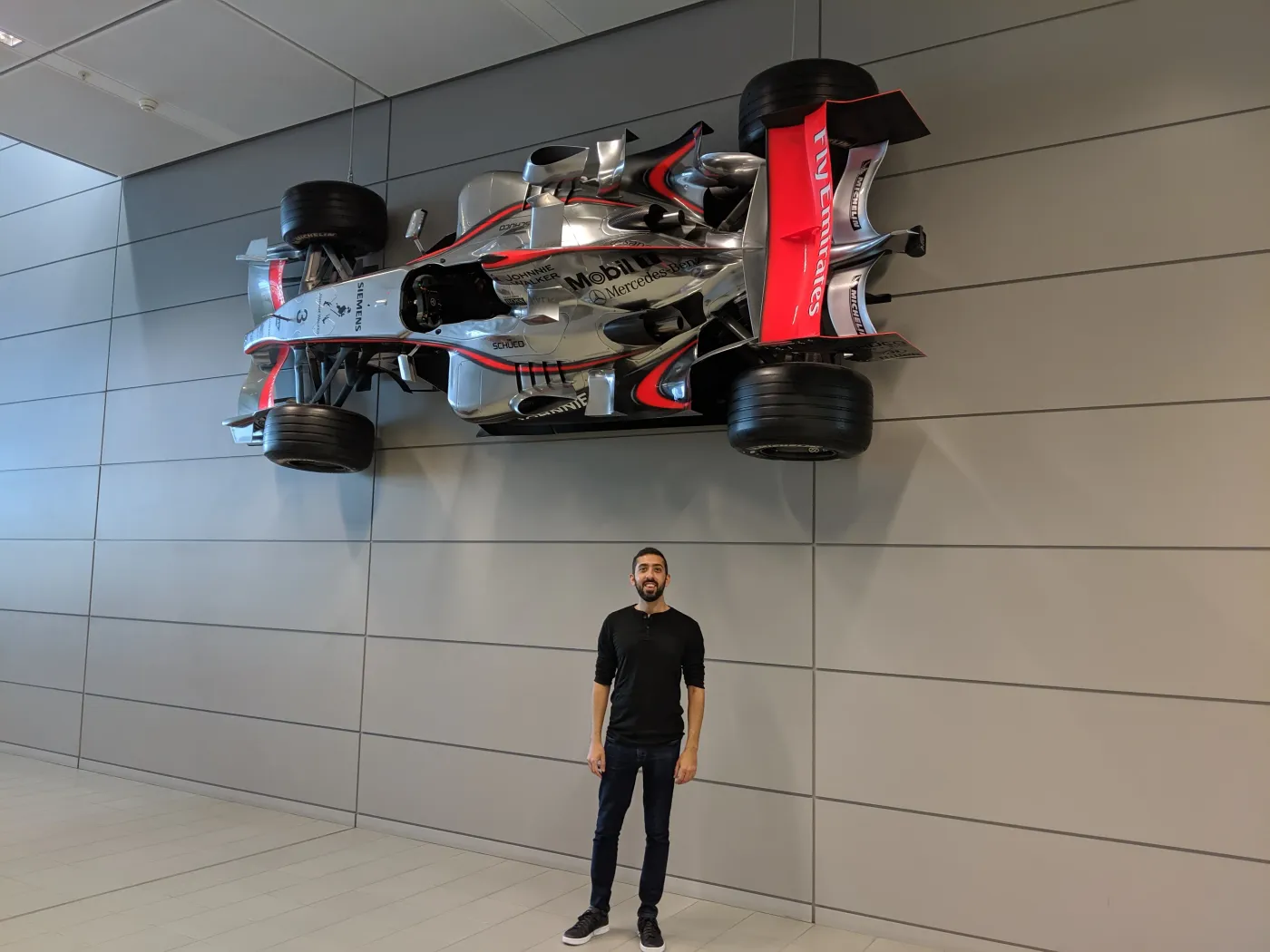 Jimmy Dushku standing beneath a silver and red McLaren Formula 1 car mounted on the wall of the Technology Centre