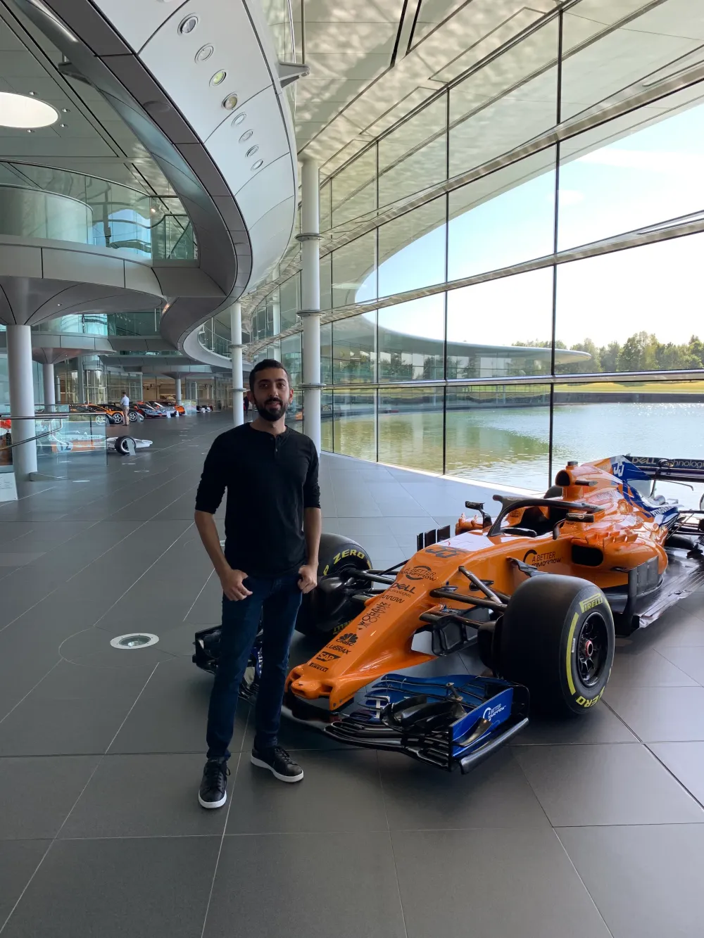 Jimmy Dushku standing beside Fernando Alonso's orange MCL33 Formula 1 car inside the McLaren Technology Centre Boulevard