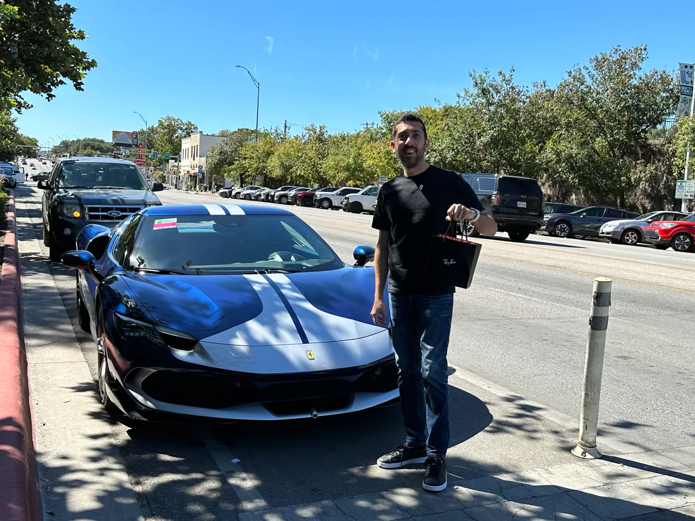 Jimmy Dushku holding a Ray-Ban bag next to Charles Leclerc's parked Ferrari 296